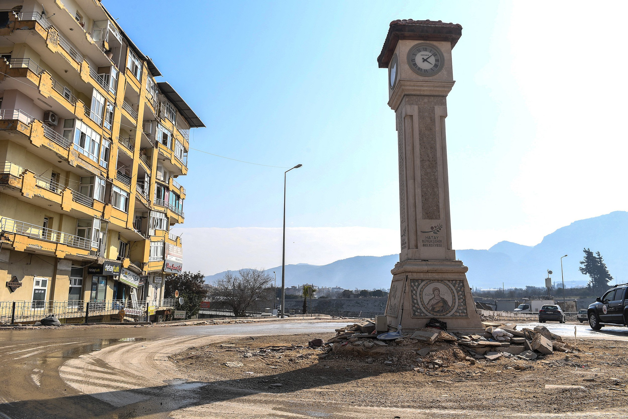 Ngôi nhà bên trái bị động đất xé rách, nghiêng ngả chực đổ sập. Bên phải, ngọn tháp biểu tượng của thành phố Antakya vẫn đứng vững. (Ảnh: Thành Đạt)