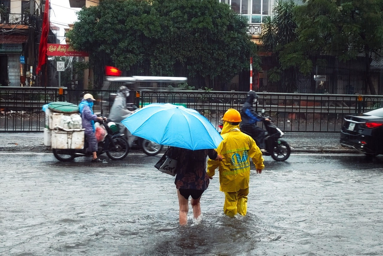 Công nhân thoát nước đưa người dân vượt qua điểm úng ngập trên đường Giải Phóng.