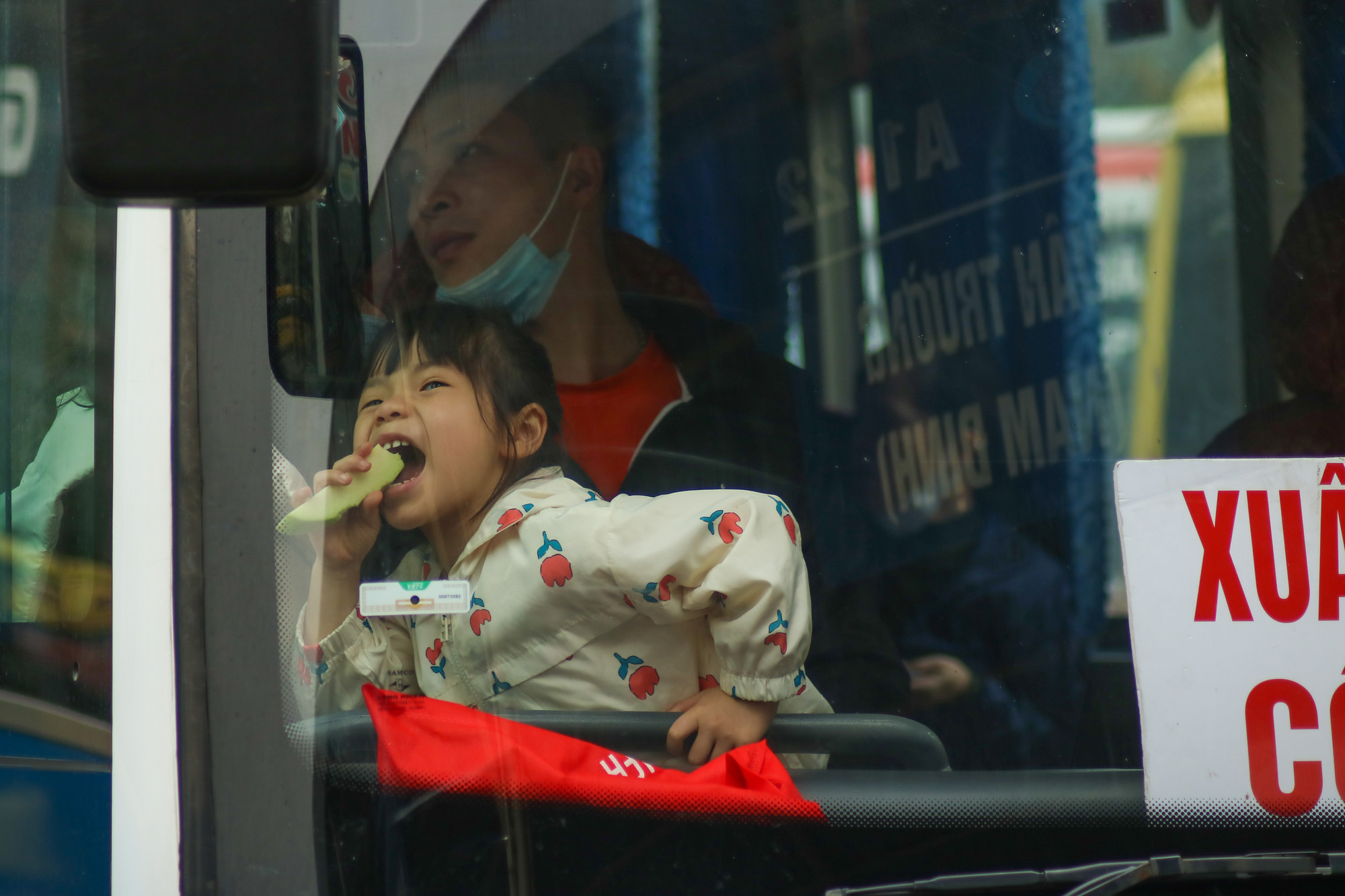 Một bé gái vui vẻ và háo hức khi xe chuẩn bị lăn bánh, đưa cả gia đình về với nơi quê nhà.