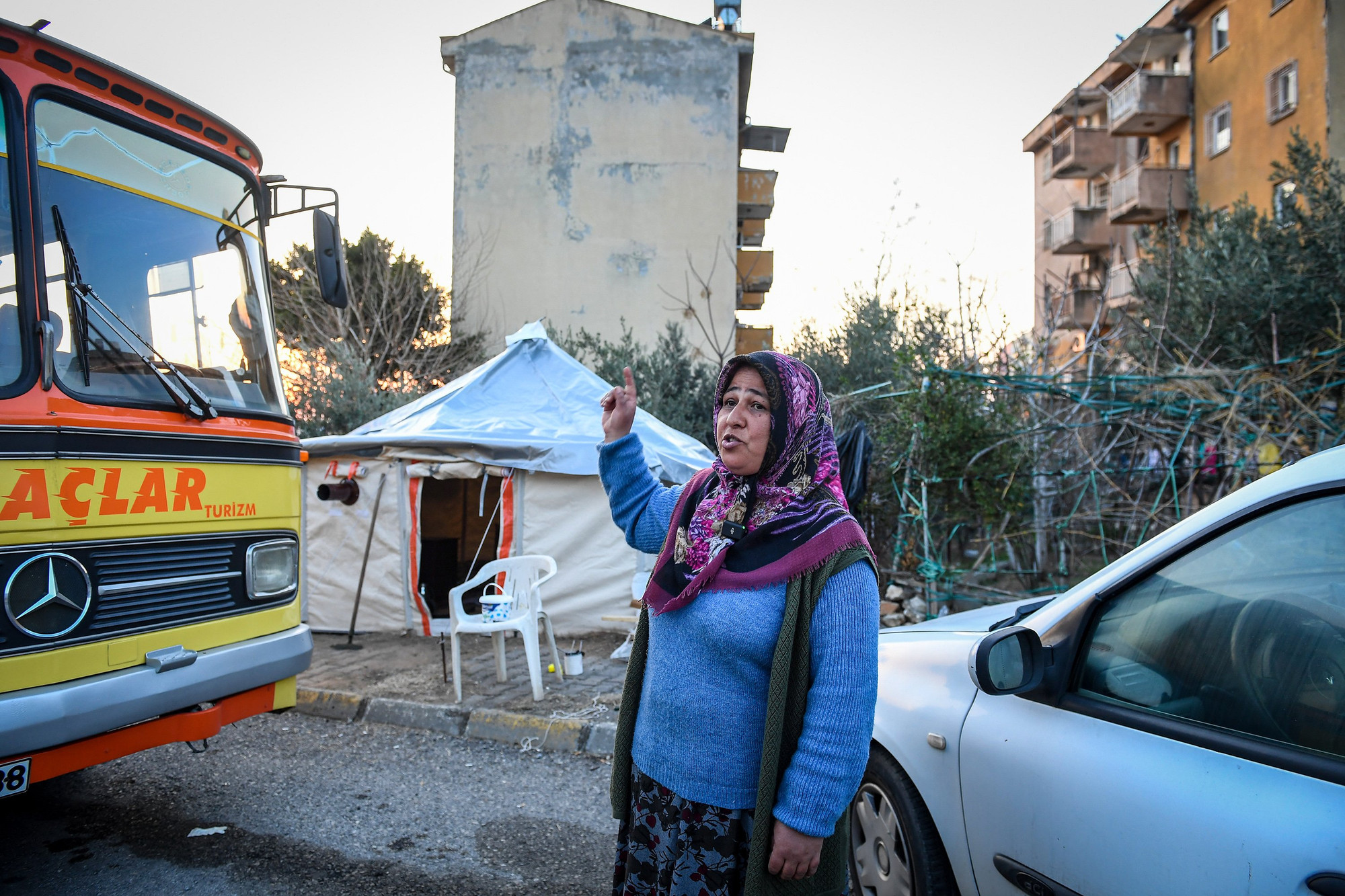 Bà Emine Bozlurt bên chiếc lều tạm và chiếc xe buýt tạm trú của gia đình mình những ngày sau động đất. (Ảnh: Thành Đạt)