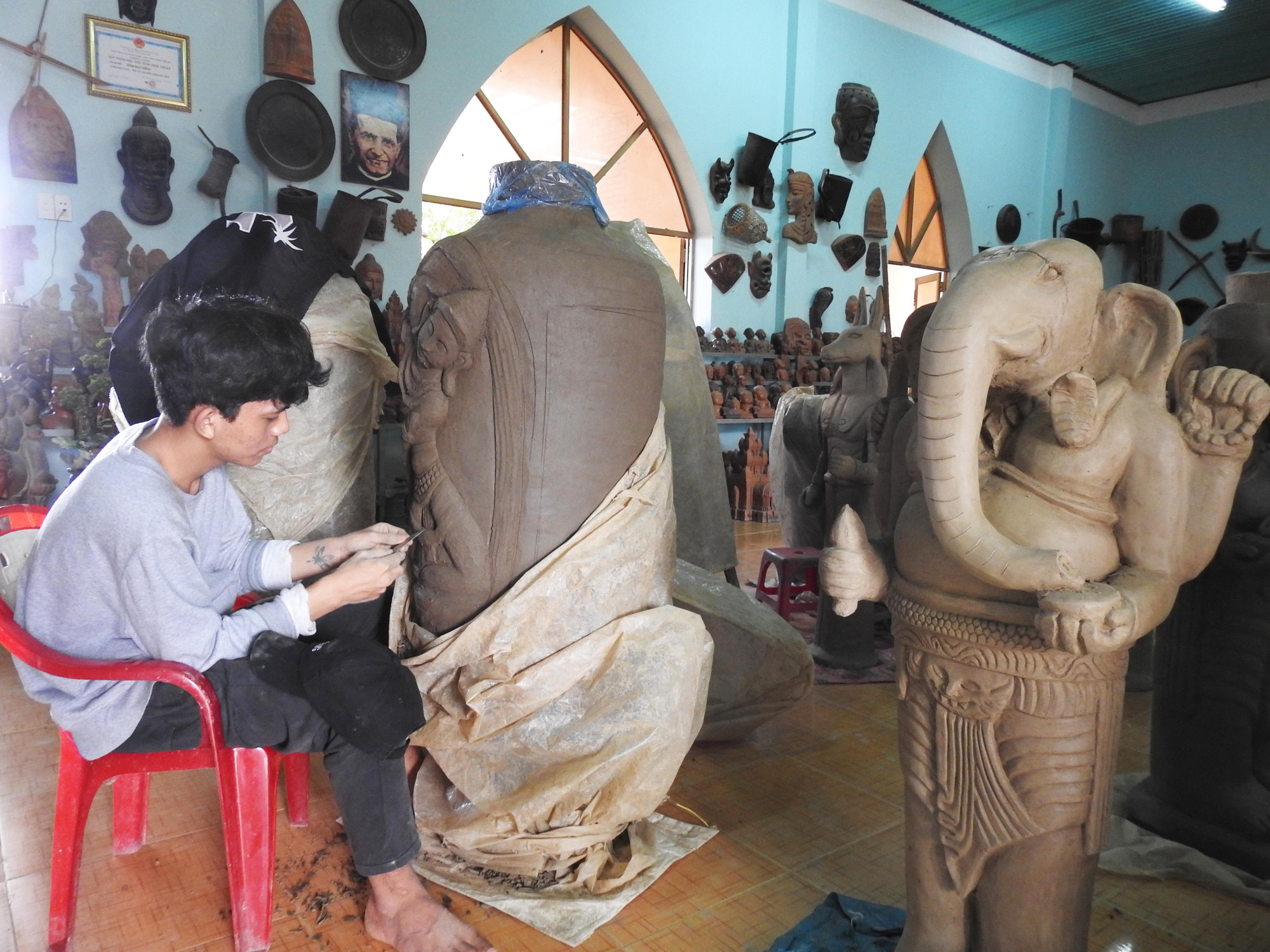 Thanh niên trẻ Đàng Tuấn Khang ( Ninh Thuận) đang chạm trổ tượng nữ thần dân tộc Chăm trên chiếc bình được chế tác gốm mỹ nghệ theo đơn đặt hàng. (Ảnh: Nguyễn Trung)
