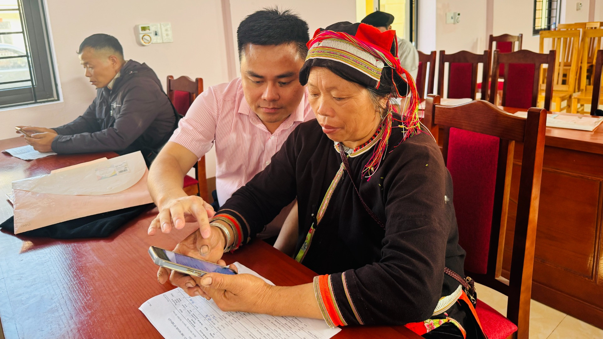 Cán bộ tín dụng hướng dẫn bà con cách truy cập ứng dụng của Ngân hàng Chính sách xã hội trên điện thoại để tra cứu các khoản vay.