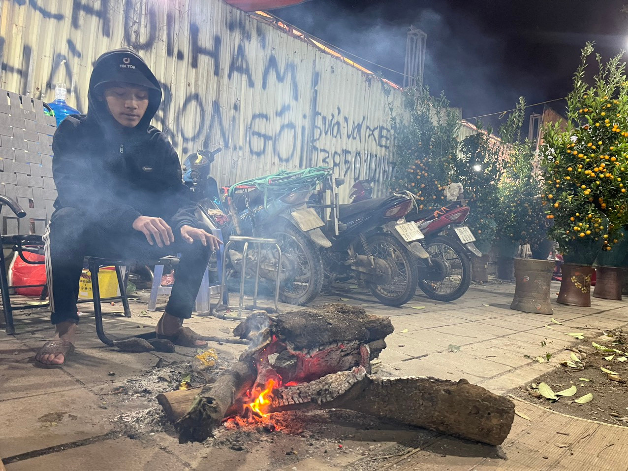 Đêm 22/1, thời tiết ngoài trời hạ xuống chỉ còn 7-8 độ C. Trên vỉa hè đường Nguyễn Chánh (Hà Nội), anh Đinh Công Văn (quê Thanh Sơn, Phú Thọ) phải nhóm lửa đốt để sưởi ấm. Từ vài hôm trước, anh Văn đã cùng gia đình mang đào, quất xuống Thủ đô để bán dịp Tết.