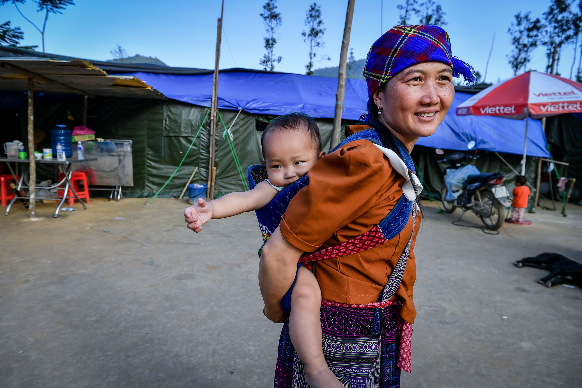 Sau thảm họa sạt lở hồi đầu tháng 9, họ đã quen dần với nhịp sống mới. Trong ảnh, chị Thào Thị Đậu, năm nay 21 tuổi cõng theo bé Lý Seo Tung thẩn thơ trên khu tạm cư trên ngọn đồi tại xã Nậm Lúc. Vẫn chưa kịp hoàn hồn sau thảm họa sạt lở tại Nậm Tông, chị Thào cho biết: Giờ chị chỉ mong sớm có nhà mới để ổn định cuộc sống.