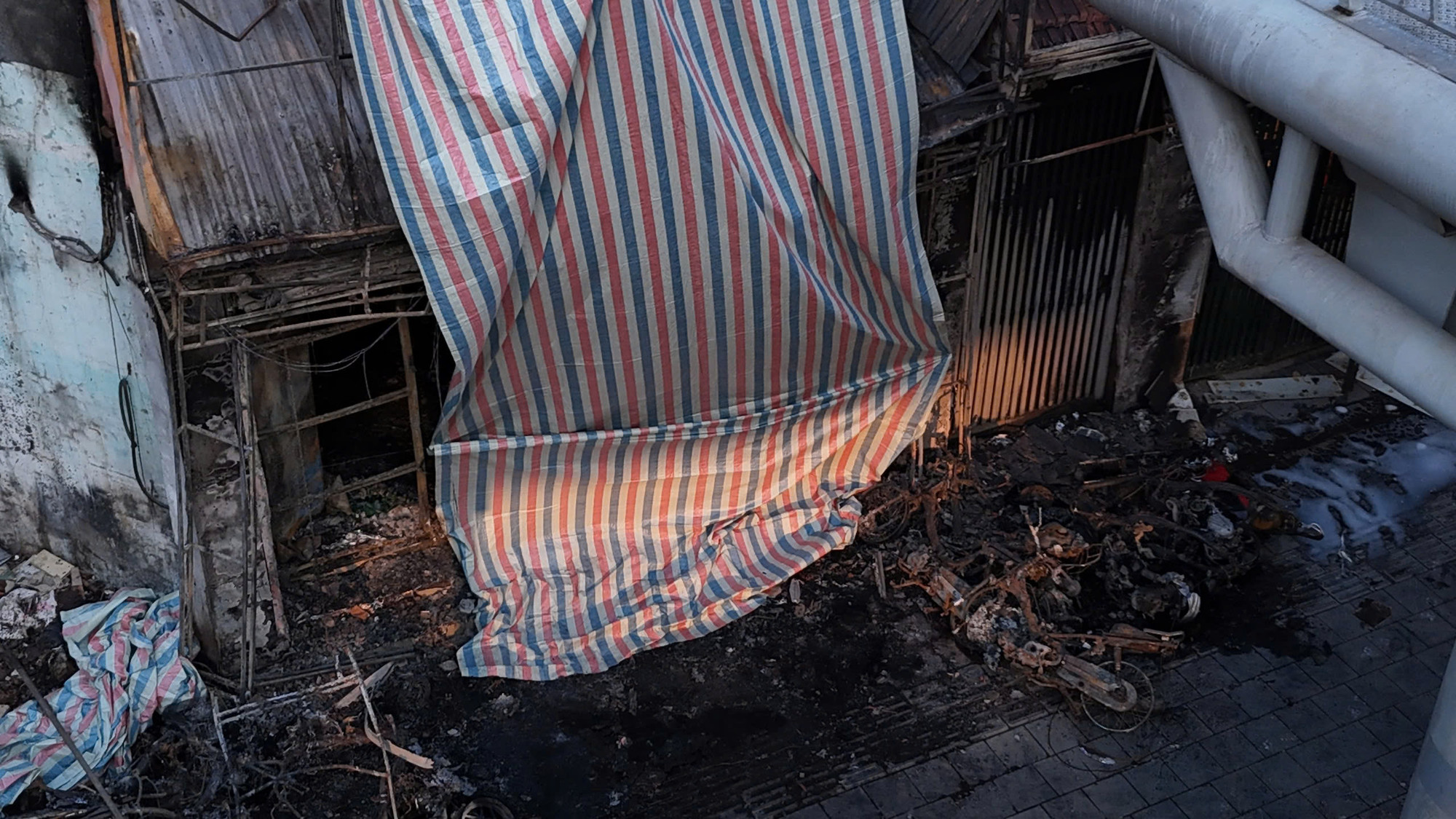 Mặt ngoài hiện trường được phủ một lớp bạt. Có thể thấy rõ những xác xe máy cháy rụi cả khung.