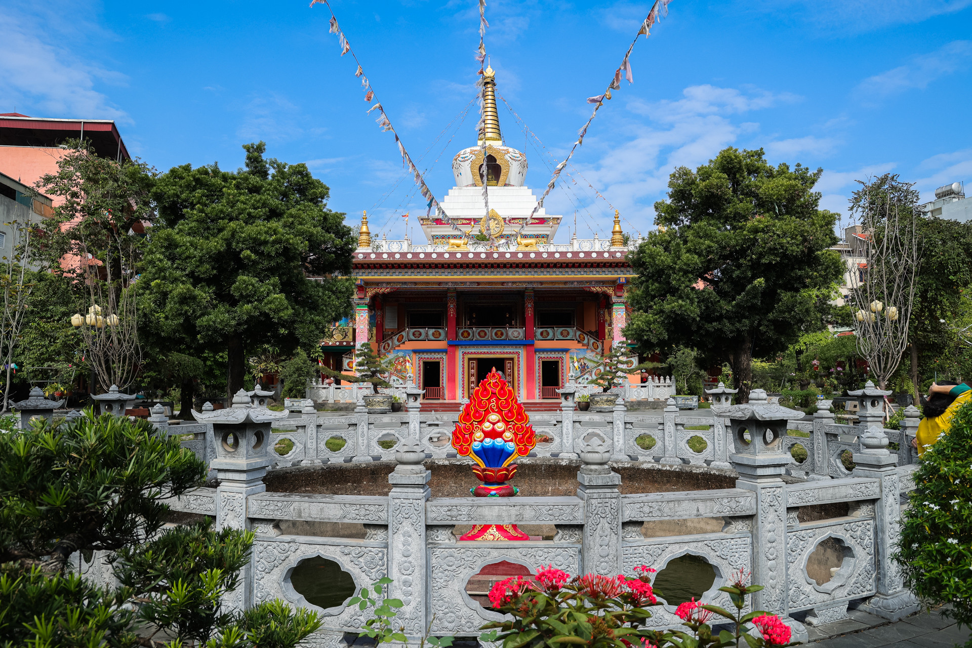 Giếng chùa trước cổng được bao quanh bởi hàng lan can bằng đá đẹp và tinh tế. Nổi bật nhất là biểu tượng Tài bảo màu đỏ rực rỡ, biểu hiện sự cúng dường và cũng là sự cầu nguyện có đủ tư lương để tu tập.