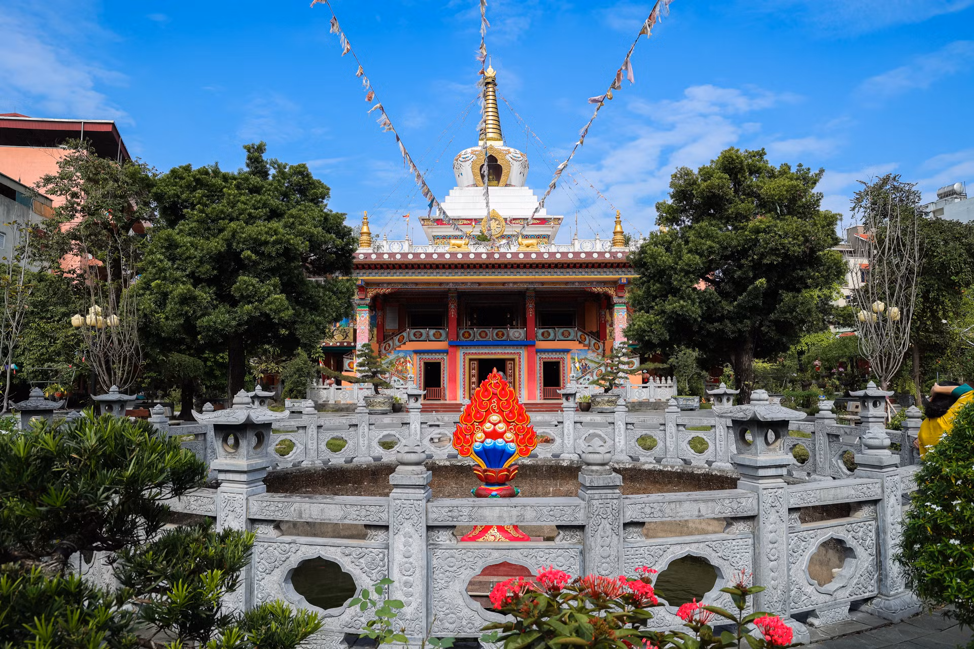 Giếng chùa trước cổng được bao quanh bởi hàng lan can bằng đá đẹp và tinh tế. Nổi bật nhất là biểu tượng Tài bảo màu đỏ rực rỡ, biểu hiện sự cúng dường và cũng là sự cầu nguyện có đủ tư lương để tu tập.
