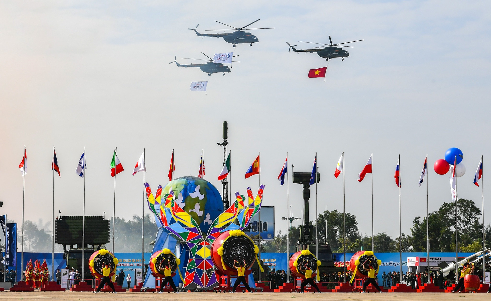 Trực thăng của lực lượng Không quân Việt Nam mang cờ Tổ quốc và cờ triển lãm bay qua lễ đài. Trực thăng của lực lượng Không quân Việt Nam mang cờ Tổ quốc và cờ triển lãm bay qua lễ đài.
