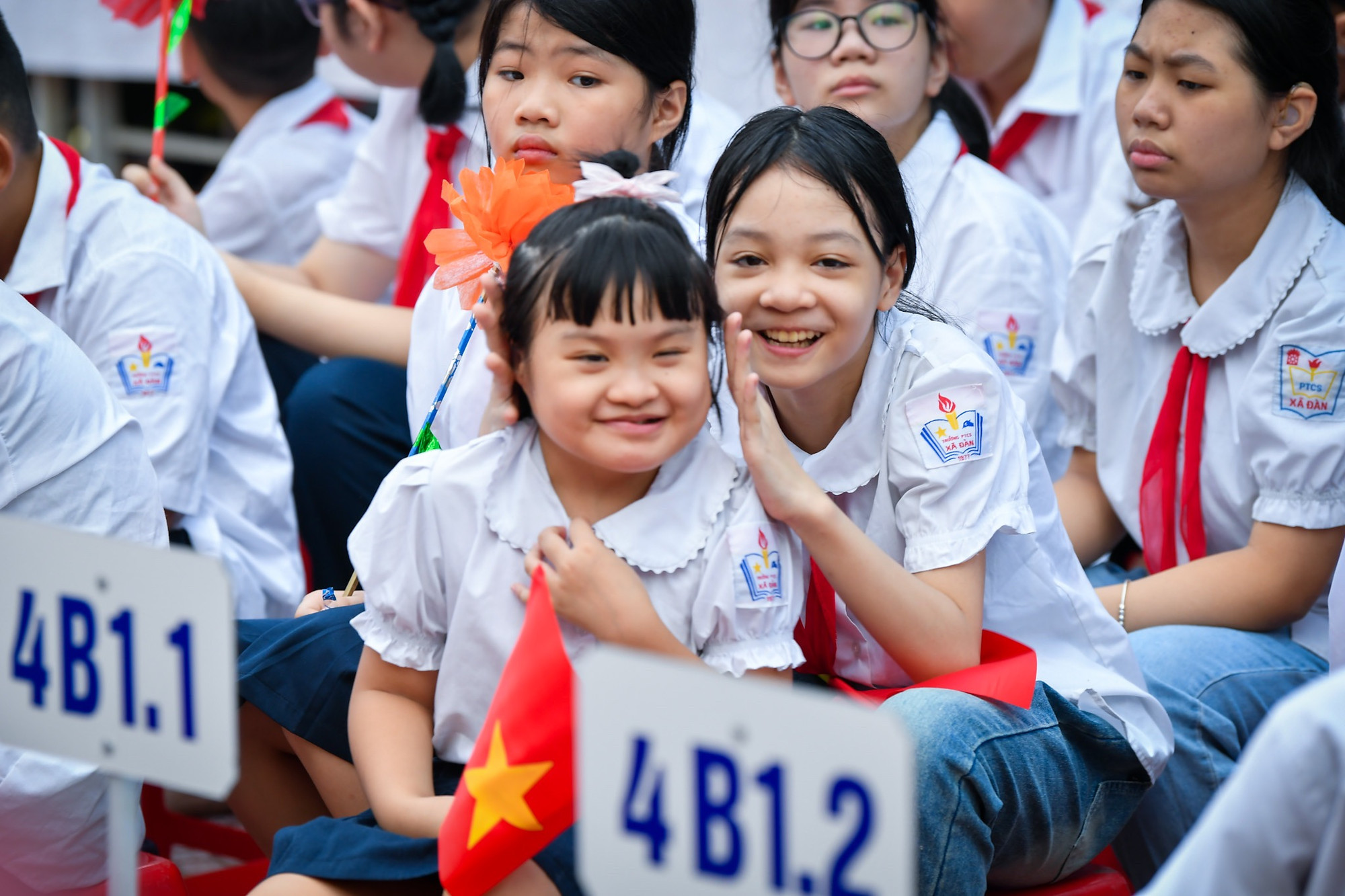 Đúng 8 giờ, tiếng trống trường vang lên báo hiệu buổi khai giảng chính thức bắt đầu. Khoảng sân phía trước, học sinh các khối đã ngồi thành từng hàng ngay ngắn. Các em nói chuyện với nhau bằng cử chỉ của đôi tay, bằng ánh mắt và cả nụ cười.