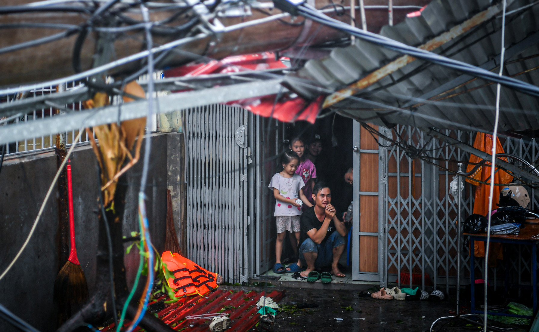 Một gia đình co ro trong căn nhà của mình. Phía trước, mái nhà làm bằng khung thép lợp tôn đã bị siêu bão "vò nát", méo mó...