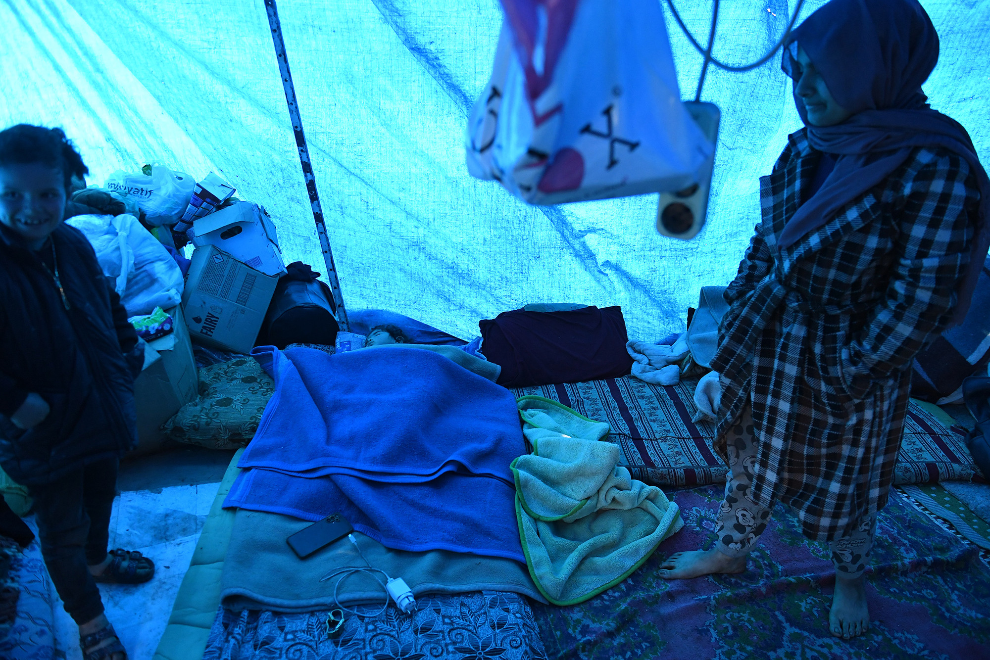 Bên trong căn nhà tạm cư của những nạn nhân động đất chỉ chủ yếu là chăn màn và quần áo cùng vài thùng nước lấy về từ các điểm cứu trợ.