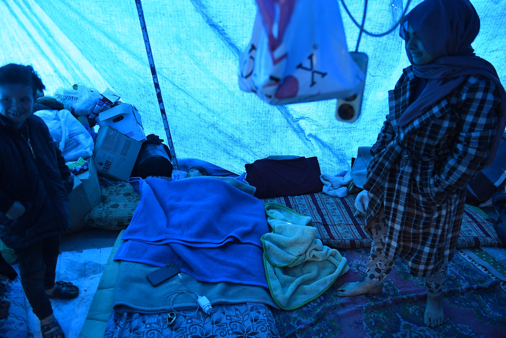 Bên trong căn nhà tạm cư của những nạn nhân động đất chỉ chủ yếu là chăn màn và quần áo cùng vài thùng nước lấy về từ các điểm cứu trợ.