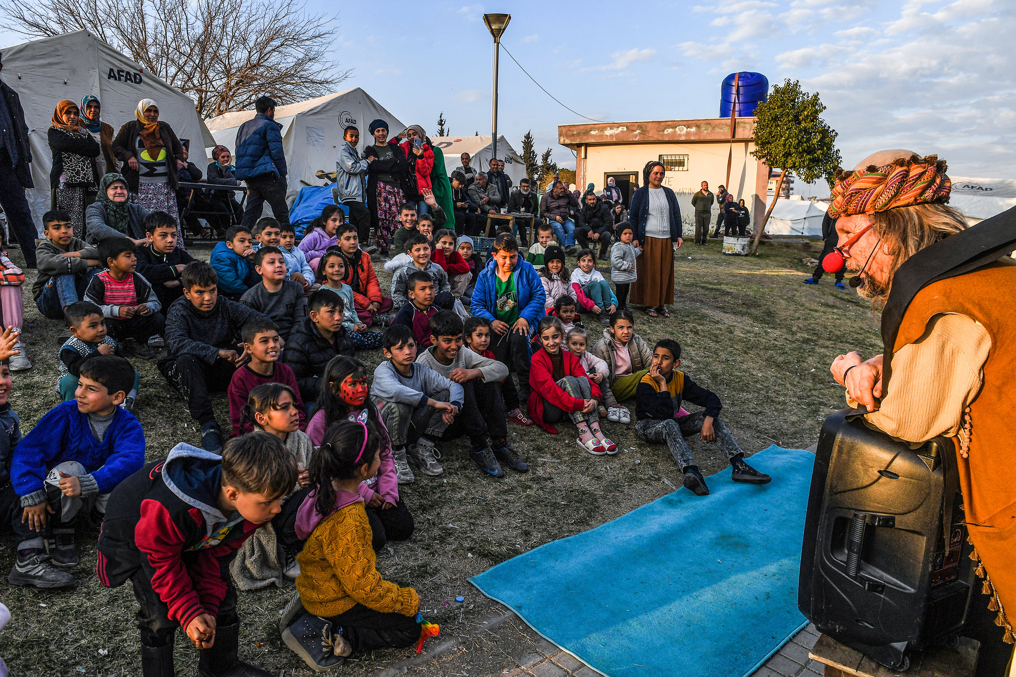 Hơn 20 đứa trẻ đang quây lại cuối con đường, gần sát khu vực phát đồ ăn tối. Từ cabin, Mehmet Tahir bật nhạc hiệu của gánh xiếc, tay bóp chiếc còi dùng trong các lễ hội. Lũ trẻ nghe thấy liền nháo nhác chạy lại, vây kín chiếc xe đã đỗ gọn bên lề đường.