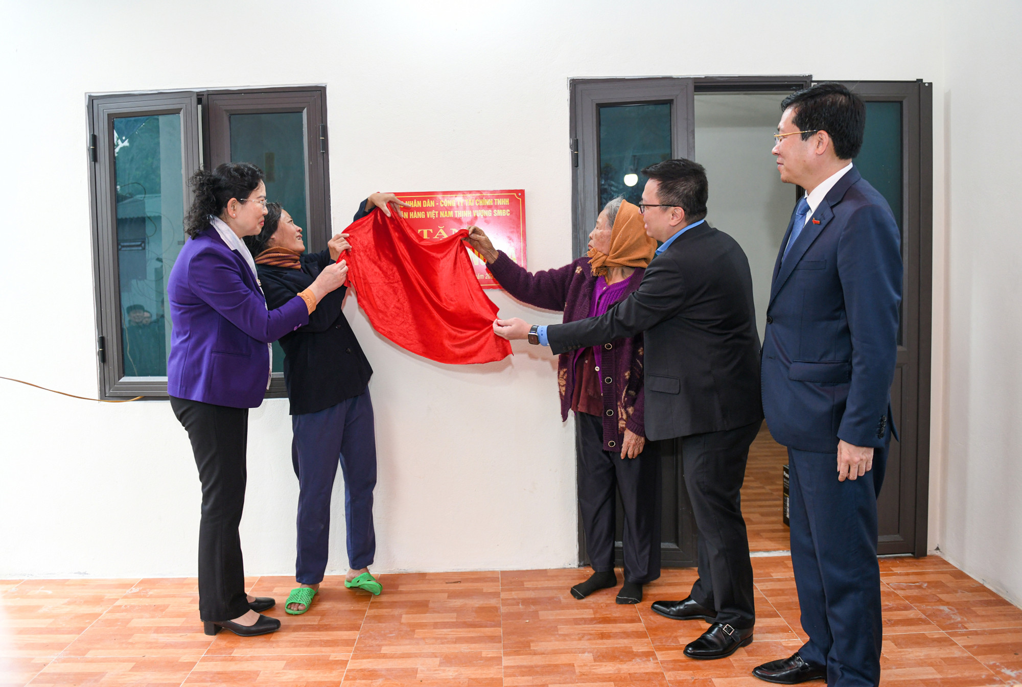 Các đồng chí cùng gia đình bà Bồ Thị Gái mở biển bàn giao một trong năm ngôi nhà mới.