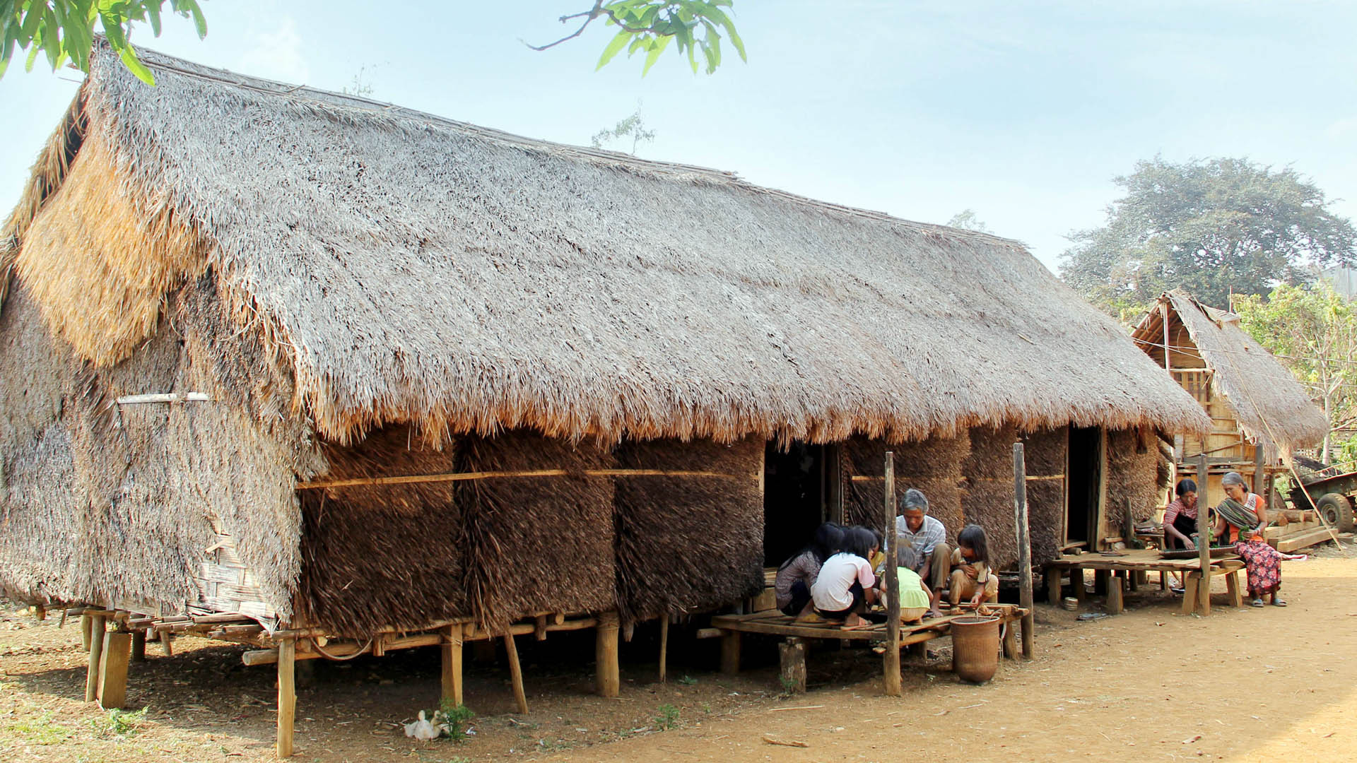 Già K'Diệp trò chuyện cùng lũ trẻ trước cửa nhà dài truyền thống người Mạ.