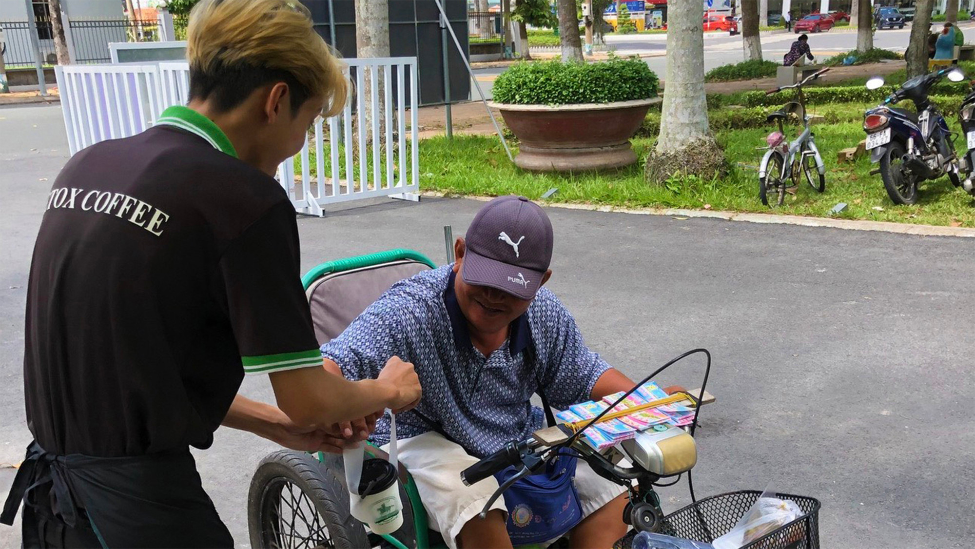 Nhân viên quán cà-phê treo mang cà-phê phục vụ người bán vé số.