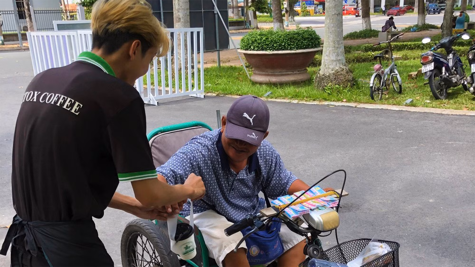 Nhân viên quán cà-phê treo mang cà-phê phục vụ người bán vé số.