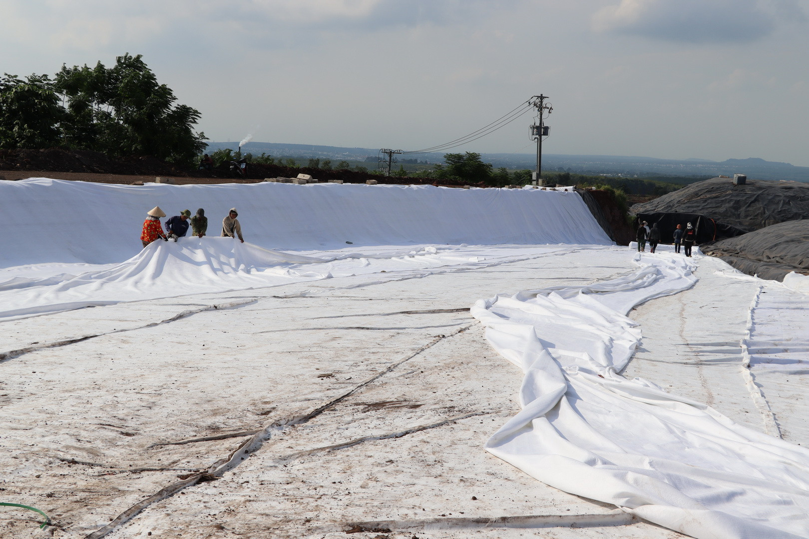 Công nhân lót bạt dưới đáy hố chôn lấp chất thải trơ sau xử lý.