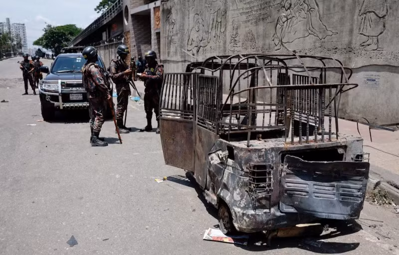 Quân đội Bangladesh bên cạnh một chiếc xe kéo bị đốt cháy trong bối cảnh bạo lực bùng phát sau các cuộc biểu tình của sinh viên, Dhaka, Bangladesh, ngày 19/7/2024. (Ảnh: Reuters)