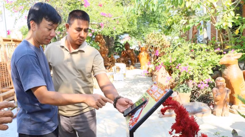 Kỹ thuật viên hướng dẫn người dân sử dụng điện thoại thông minh kết nối với bảng có công nghệ kết nối không dây tầm ngắn để tìm hiểu thông tin về các điểm du lịch tại Ninh Thuận, chọn nơi tham quan và trải nghiệm khi đến địa phương.