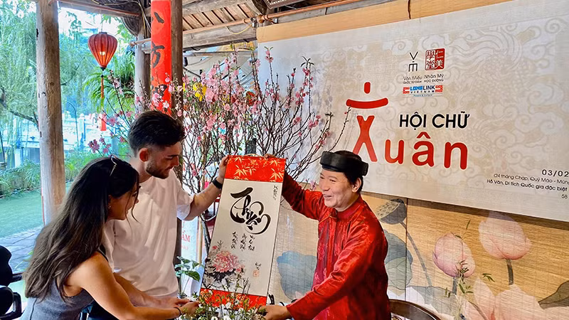 Một "thầy đồ" hiện đại trao bức thư pháp chữ quốc ngữ tặng du khách nước ngoài trong ngày đầu Xuân tại Văn Miếu-Quốc Tử Giám (Hà Nội). 