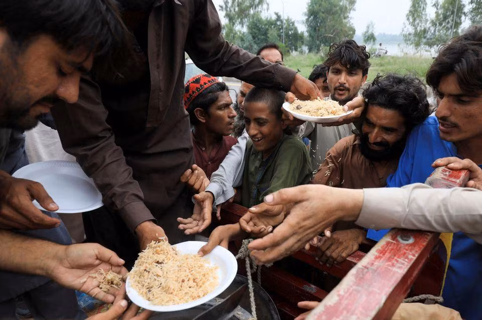 Người dân vùng lũ tại Charsadda nhận cơm từ nhân viên cứu hộ. (Ảnh: Reuters)
