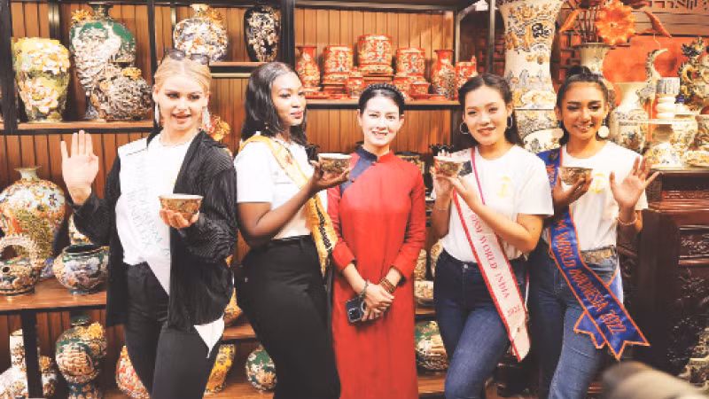 Nghệ nhân Vũ Như Quỳnh (đứng giữa) giao lưu với khách tham quan là những người đẹp tham gia cuộc thi Hoa hậu Du lịch quốc tế năm 2022 tại một cuộc triển lãm.