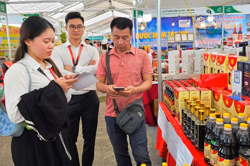 Nhân viên ngân hàng hỗ trợ người mua, bán hàng ứng dụng công nghệ thanh toán không dùng tiền mặt.