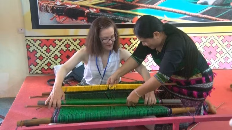 Du khách nước ngoài thích thú khi được nghệ nhân người M’nông giới thiệu, trực tiếp hướng dẫn các thao tác dệt thổ cẩm.