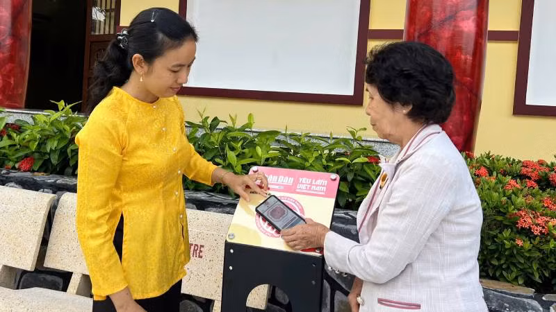 Nhân viên Khu lưu niệm Nguyễn Thị Định hướng dẫn khách du lịch cách kết nối với trạm tương tác thông minh bằng điện thoại. (Ảnh: HOÀNG TRUNG).