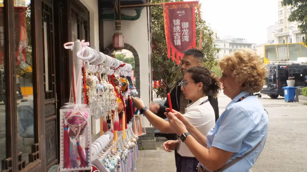 Thành viên của đội đua xe đạp tranh thủ mua quà lưu niệm ở Cẩm Tú cổ trấn-điểm du lịch cấp 4A của Trung Quốc.