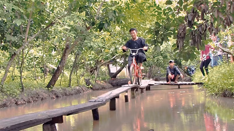 Khách du lịch trải nghiệm đạp xe qua cầu ván tại làng du lịch Mỹ Khánh. 