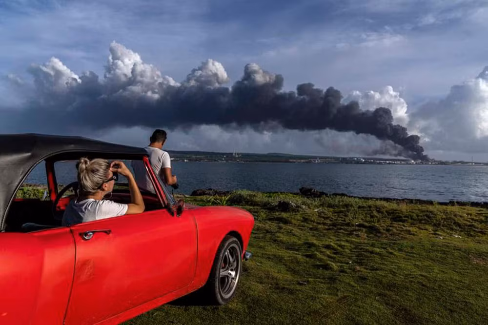 Ngọn lửa lan rộng ở thành phố Matanzas, cách thủ đô Havana 90km về phía đông, nơi có ít nhất 3 thùng dầu thô bốc cháy sau khi bị sét đánh vào đêm thứ 6 vừa qua. Trong ảnh, hai người dân quan sát thấy cột khói khổng lồ bốc lên từ kho nhiên liệu tại thành phố ven biển này. (Ảnh: AP)