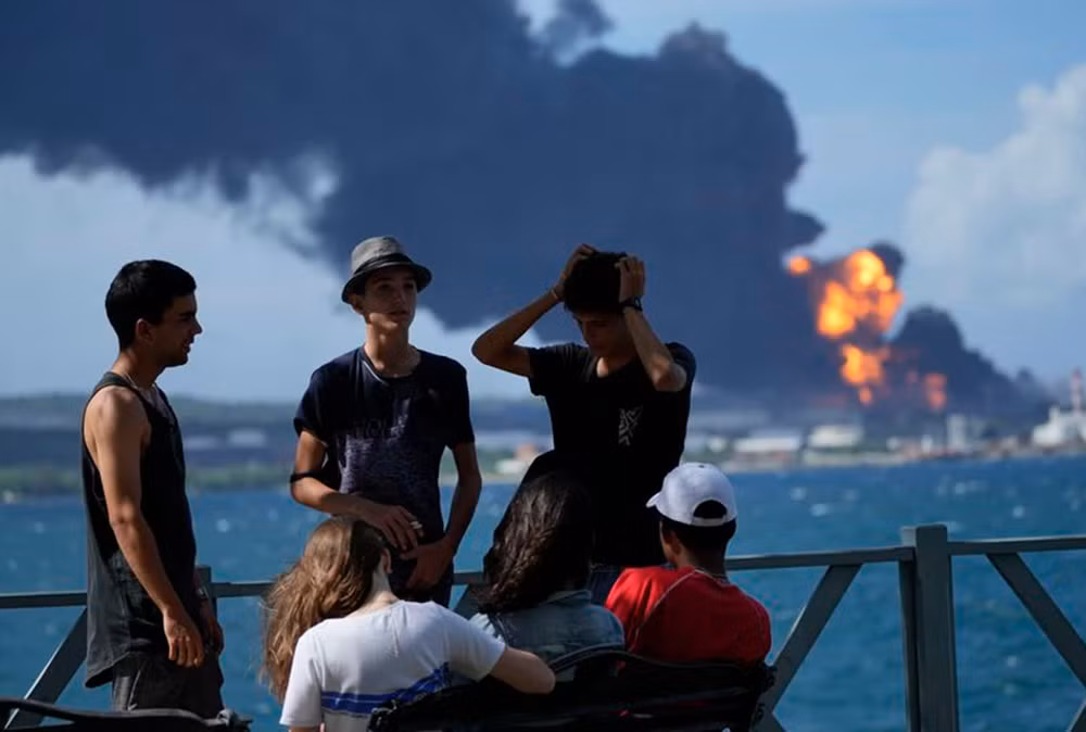 Nhóm thanh niên tụ tập trên một bến tàu trong khi lửa và khói vẫn tiếp tục bốc lên từ Căn cứ siêu tàu Matanzas. (Ảnh: AP)