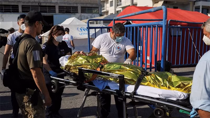 Nhân viên cứu nạn đưa người di cư lên xe cứu thương. (Ảnh: Reuters)