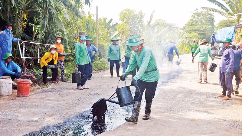 Các thành viên của Đội vá đường thiện nguyện huyện Chợ Mới đổ nhựa đường, thi công đoạn đường nông thôn xuống cấp.