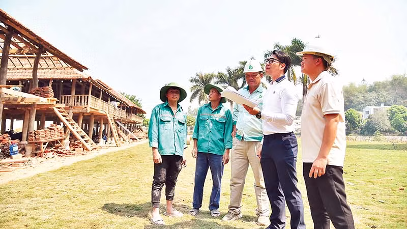 Anh Bùi Anh Tiến (người đeo kính) trao đổi với công nhân thi công dãy nhà sàn của người Thái cổ. (Ảnh MỸ HÀ)