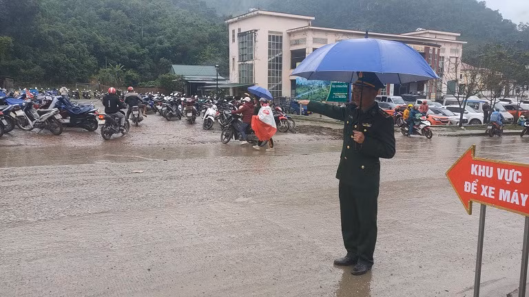 Cán bộ đồn Biên phòng cửa khẩu quốc tế Nậm Cắn đội mưa hướng dẫn người dân ra, vào chợ.