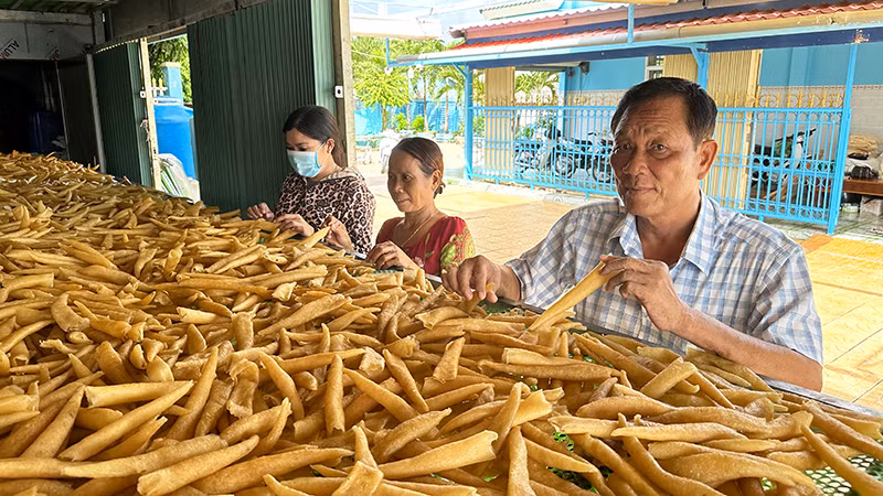 Thương binh Trần Văn Khi hướng dẫn lao động dân tộc Khmer cách chế biến đặc sản bong bóng cá biển. (Ảnh NGUYỄN PHONG)