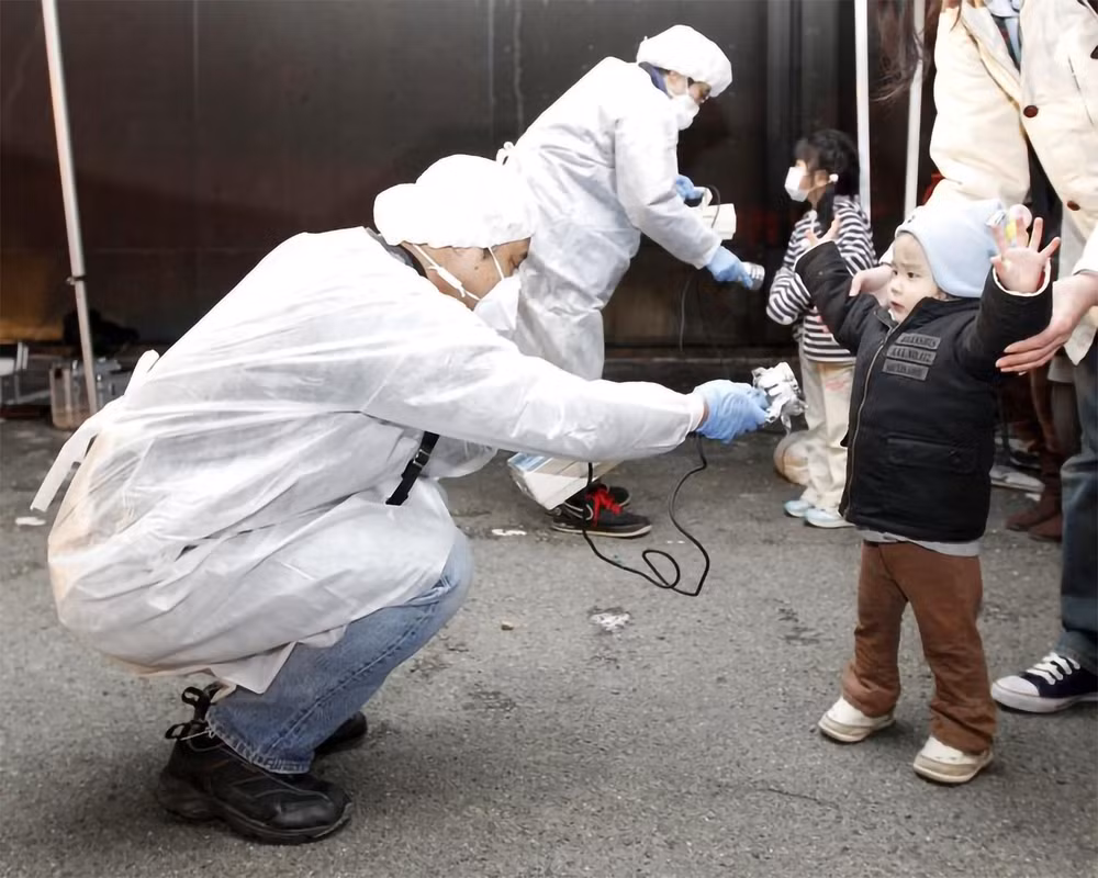 Tại nhà máy điện hạt nhân Fukushima Daiichi ở tỉnh Fukushima, sóng thần đã tràn qua các hệ thống bảo vệ và làm ngập các lò phản ứng, gây ra thảm họa nghiêm trọng. Thảm họa đã làm tê liệt nhà máy điện Fukushima Daiichi, buộc hơn 160.000 cư dân phải sơ tán vì rò rỉ phóng xạ trong không khí. Trong ảnh: Các nhân viên mặc đồ bảo hộ kiểm tra dấu hiệu nhiễm phóng xạ đối với trẻ em đến từ khu vực phải sơ tán gần nhà máy điện hạt nhân Fukushima Daini ở thành phố Koriyama, ngày 13/3/2011. (Ảnh: Reuters)