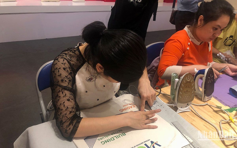 Một thợ thủ công của Vụn Art đang trổ các họa tiết trang trí bằng lụa trên túi vải với đầu mũi kéo.