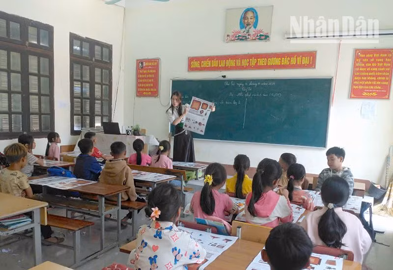 Giáo viên Trường tiểu học Ngọc Chiến, huyện Mường La hướng dẫn học sinh cách cắt, ghép mô hình Cột cờ Hà Nội từ ấn phẩm đặc biệt của Báo Nhân Dân.