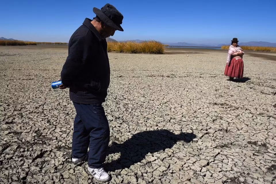 Ông Gabriel Flores và bà Isabel Apaza đi bộ trên lòng hồ Titicaca khô nứt trong mùa hạn hán. Ảnh: Reuters.