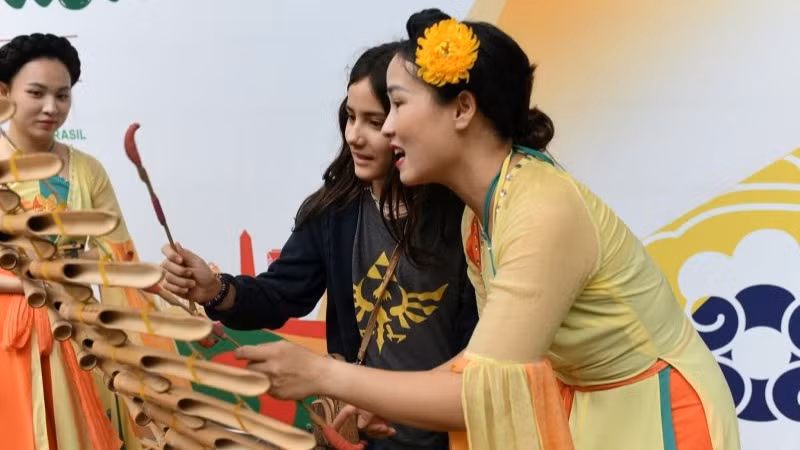 Cô gái trẻ Brazil thử chơi nhạc cụ dân tộc Việt Nam. (ẢNH: BTC)