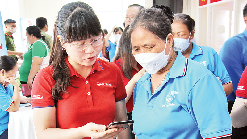 Nhân viên Agribank Chi nhánh Nhà Bè hướng dẫn người dân huyện Nhà Bè (Thành phố Hồ Chí Minh) thao tác thanh toán không dùng tiền mặt. (Ảnh Thế Anh)