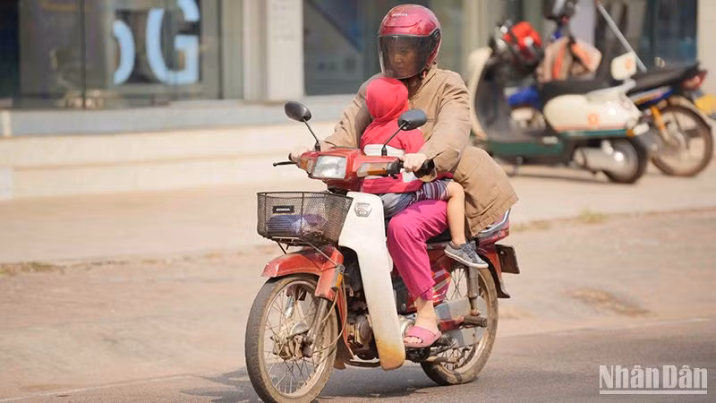 Người dân Lào tìm cách hạn chế nắng nóng khi tham gia giao thông. Ảnh: Hải Tiến