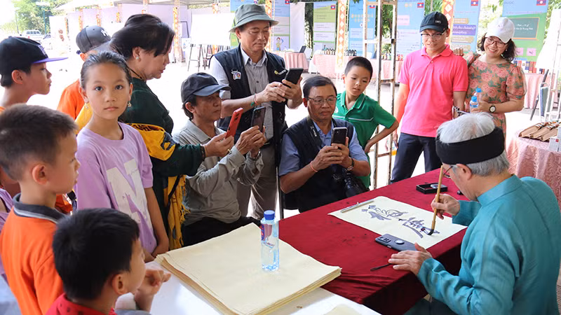 Các em học sinh và người dân hai nước thích thú thưởng thức nghệ thuật thư pháp tại sự kiện. (Ảnh: Hải Tiến)