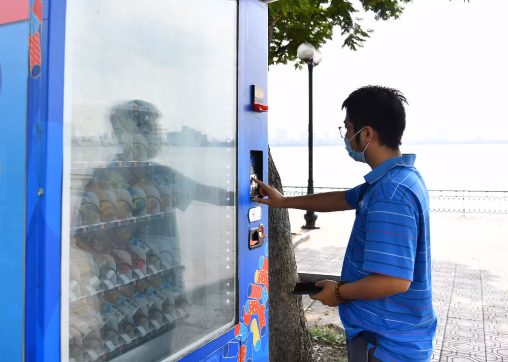 Người dân mua nước uống có đường tại máy bán nước tự động trên địa bàn thành phố Hà Nội. (Ảnh MỸ HÀ) 