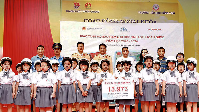 Đại diện các đơn vị trao tặng mũ bảo hiểm cho học sinh lớp 1 Trường tiểu học Hồng Thái. (Ảnh: LÝ THU)