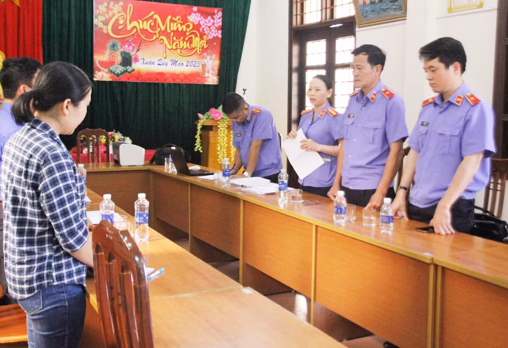 Phan Thị Anh (bên trái) đang nghe cơ quan chức năng tống đạt quyết định khởi tố.